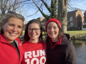 three smiling ladies participating in RUN 100 in February challenge in nice building and trees in the background